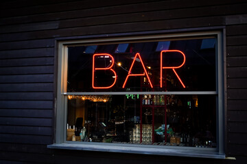 Bar sign in red neon light in a window on a dark wall