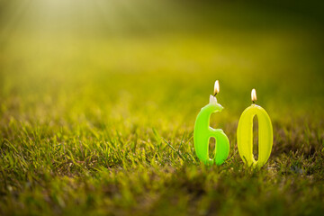 Candles in the form of numbers sixty on a green summer background.Burning candles for the 60th...