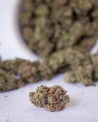 Cannabis buds trimmed and dried spilling out of a bowl with light background