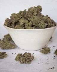 Cannabis buds trimmed and dried spilling out of a bowl with light background