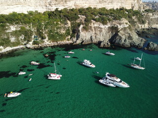 Fototapeta na wymiar Aerial panoramic view of seascape with crystal clear azure sea and rocky shores. Yachts in a beautiful lagoon on backdrop of rocks. The concept of an ideal destination for summer travel and vacation.
