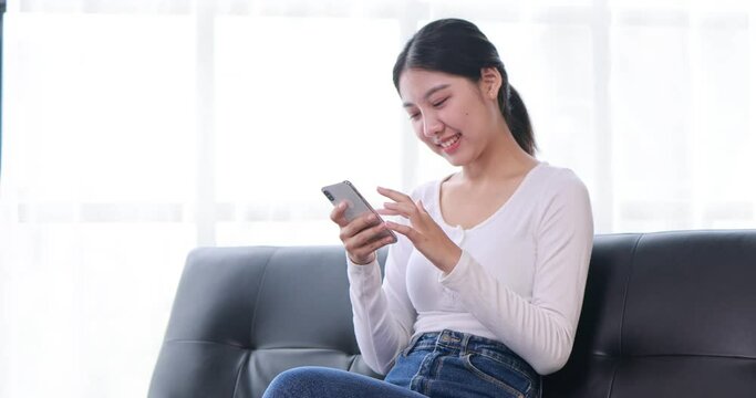 Happy millennial hispanic teen girl checking social media holding smartphone at home. Smiling young asian woman using mobile phone app playing game, shopping online, ordering delivery relax on desk.
