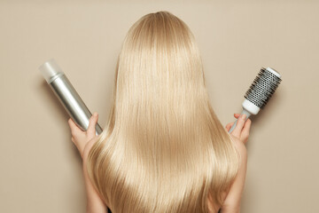 Back view of woman with long beautiful blond hair isolated on beige background holds hairdressing...