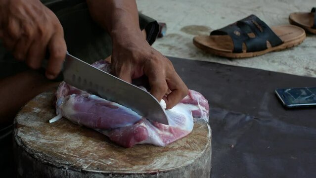 A local butcher in Indonesia cutting goat meat on a wooden cutting board