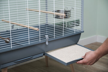 Unrecognizable personplacing tray with sepiolite, an absorbent material, into the birdcage.