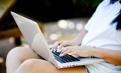 Asian woman sits with laptop in her garden at home snuggling and relaxing on her holiday.