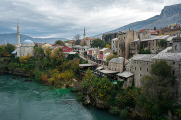 Fototapeta na wymiar Beautiful Mostar View on Fall with Islamic Mosques. Medieval Stone Houses, Souvenir Shops, Neretva River in Day. Mountains Background. Bosnia and Herzegovina.