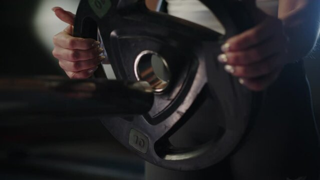 Close-up of female hands hanging a disc on a barbell. Bench press
