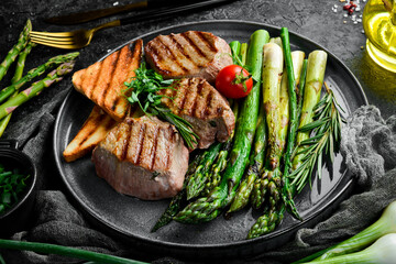 Juicy Veal steak with asparagus, tomatoes and toast. On a black stone background. Top.