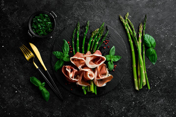 Grilled asparagus with prosciutto and basil. On a black stone background. Top view.