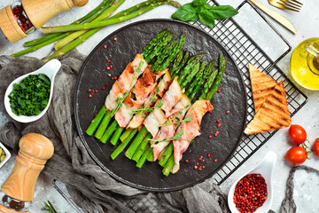 Grilled asparagus with bacon and basil on a plate. On a stone background. Top view.