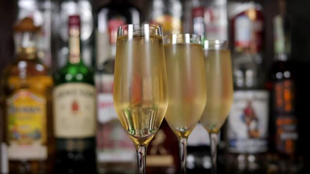 Close-up of three glasses of champagne in a bar against the background of blurred bottles with various alcohol. The concept of alcohol and holidays.