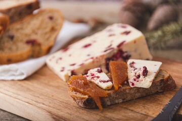 Wensleydale cheese with cranberries, red wine, honey, nuts, raisins on marble cutting board. Black concrete background. Selective focus.