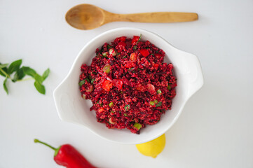 Top view of Selective focus beetroot quinoa salad with wooden spoon, fresh mint, lemon and red pepper on white table.