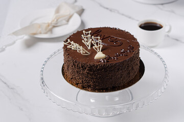 Chocolate cake on a white table on a glass tray. Chocolate cake with white chocolate decoration.
