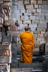 Buddhist man wearing orange robe standing in front of Sewu Temple ruins, stones. Unesco. Prambanan Temple, Central Java, Yogyakarta, Indonesia.