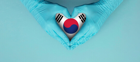 Doctors hands wearing blue surgical gloves making hear shape symbol with south korea flag