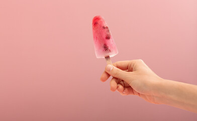 Woman hand holding an ice cream cone on a pink background.