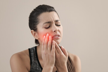 Young woman suffering from acute toothache on beige background