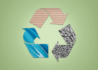 Recycling symbol made of crumpled foil, cardboard and turquoise stretch wrap on light green...
