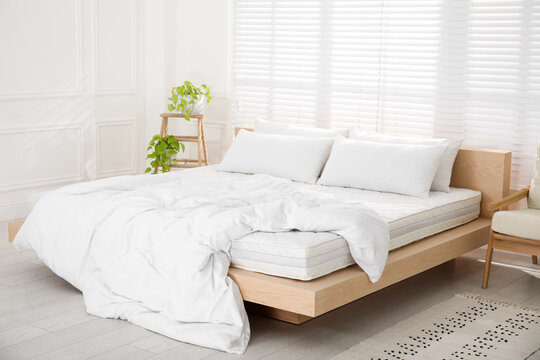 Wooden bed with soft white mattress, blanket and pillows in cozy room interior