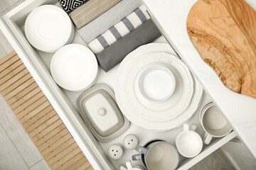 Open drawer of kitchen cabinet with different dishware and towels, top view