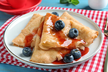 Delicious crepes served with blueberries and syrup on table, closeup