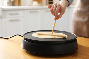 Woman cooking delicious crepe on electrical pancake maker in kitchen, closeup - obrazy, fototapety, plakaty