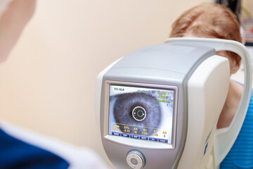 A girl optometrist examines the eyes of a patient using special modern equipment.