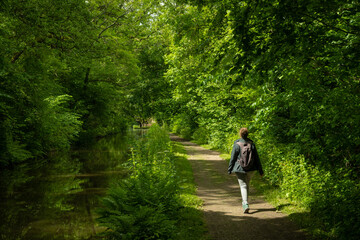 A female hiker on a footpath next to a canal in the Welsh countryside. lush green verdant trees grow in abundance in the pleasant natural surroundings of the Brecon and Monmouth canal