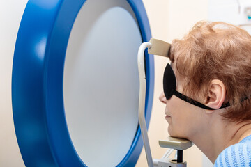 An adult girl at an ophthalmologist's appointment checks her eyesight on a special apparatus....