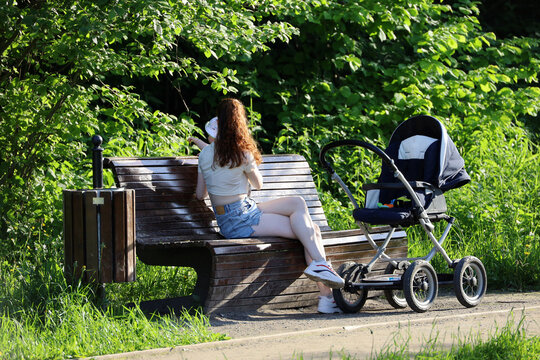 Girl with baby sitting on a bench in summer park. Young mother with child, leisure on nature