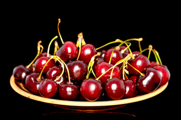 Several sweet cherries in a ceramic dish, close-up, isolated on a black background.