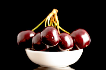 Several sweet cherries with a white ceramic saucer, close-up, isolated on a black background.