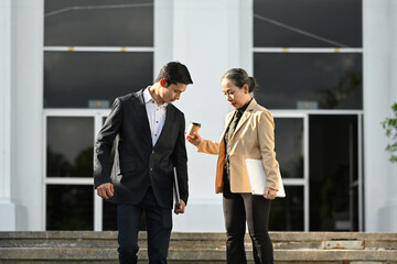 Attractive senior businesswoman and young businessman walking outside modern office building
