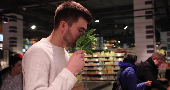 attractive young man in light jumper chooses spices and fresh herbs at the supermarket