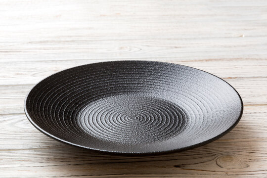 Perspective view of empty black plate on wooden background. Empty space for your design