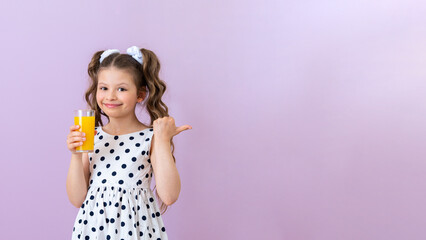 A little girl holds an orange juice and points to an advertisement on an isolated pink background....