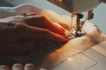 Photo of woman's hands in process of sewing linen dress using automatic sewing machine