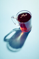 Hot tea in a glass cup with hard shadow on blue background.
