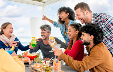 interracial group of friends at rooftop terrace bar at the beach having food and drinks celebrating...