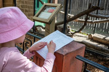 Fototapeta na wymiar Young girl completing a zoo scavenger hunt form outdoors in the spring.