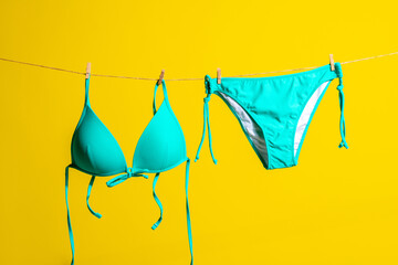 Green swimsuit hanging on a rope on a yellow background