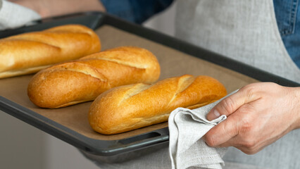 Male hands hold freshly baked french baguette in baking sheet. Bread bakery. Food background