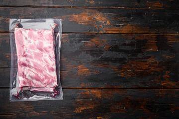 Pork ribs in a vacuum bag, on old dark  wooden table background, top view flat lay, with copy space for text