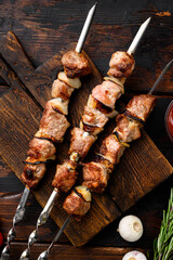 Shish kebab BBQ meat with onions and tomatoes, on old dark  wooden table background, top view flat...