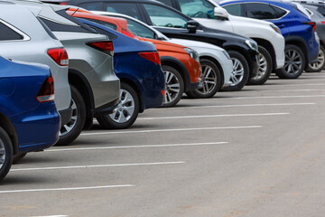 row of different color cars on asphalt parking lot at cloudy summer day with selective focus 