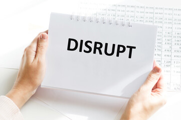 the text DISRUPT on a notebook in the hands of a person on the background of an office desk, a business concept