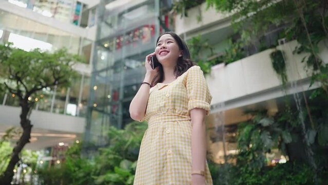 Pretty young adult asian woman stand in the middle of shopping mall calling her boyfriend, waiting at the rendezvous outside the hall, 5g internet connect people, cute asian girl talking on the phone