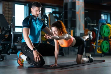 Fototapeten young woman exercising quadruplex with personal trainer in gym © goami